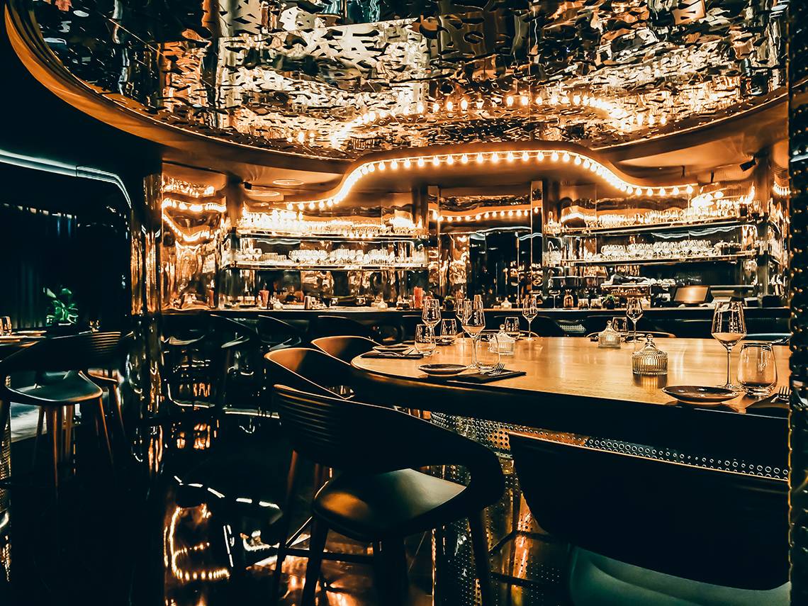 Innenansicht der Bar im Raffles The Palm Dubai mit einer runden Theke und goldenen Akzenten.