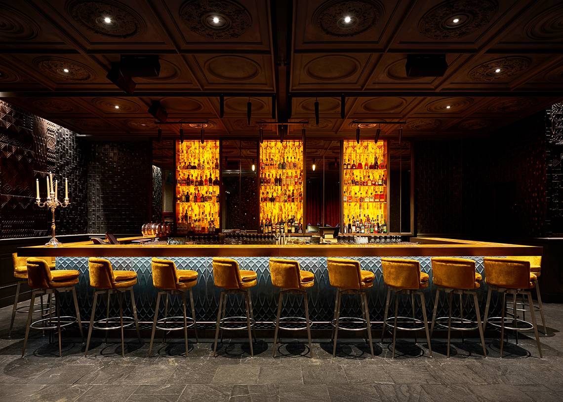 Bar-Szene im Raffles The Palm Dubai mit gelben Barhockern und einer Theke voller alkoholischer Getränke.
