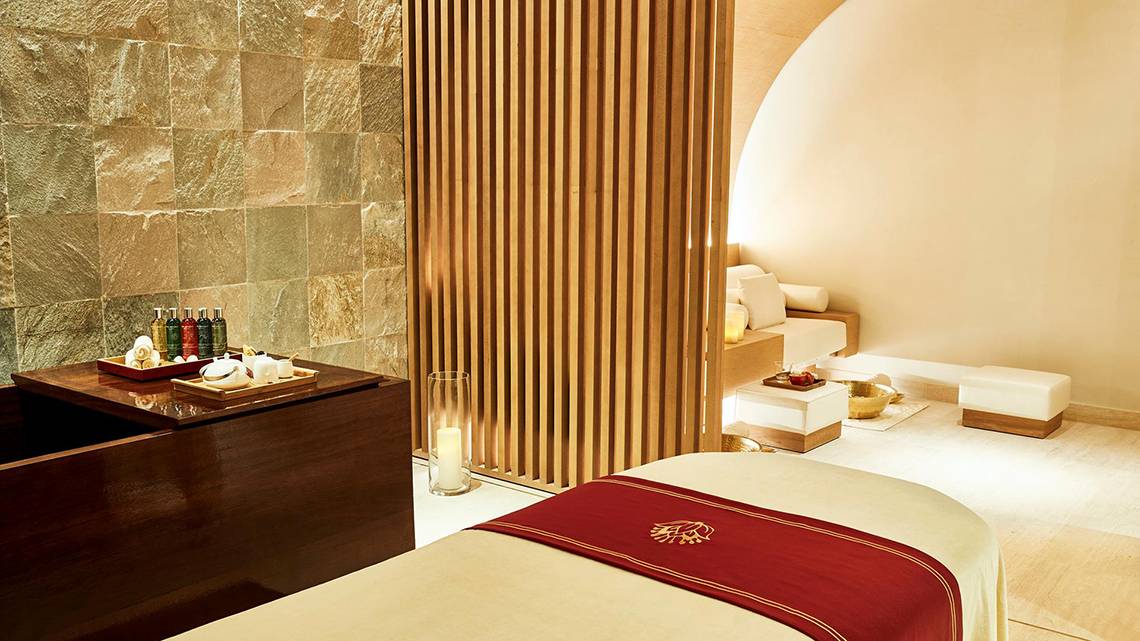 Spa-Behandlungsraum im Raffles The Palm Dubai mit Holzelementen, Sitzgelegenheiten und einem Tisch mit Wellnessprodukten.