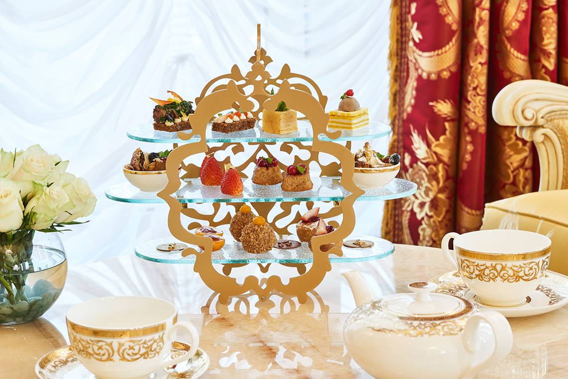 Nachmittagstee-Tafel im Raffles The Palm Dubai mit dreistöckiger Glasplatte und verschiedenen Desserts.