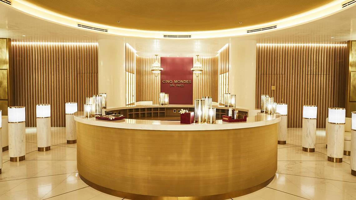 Empfangsbereich des Cing Mondes Spa im Raffles The Palm Dubai mit goldenem Tresen und weißen Säulen.