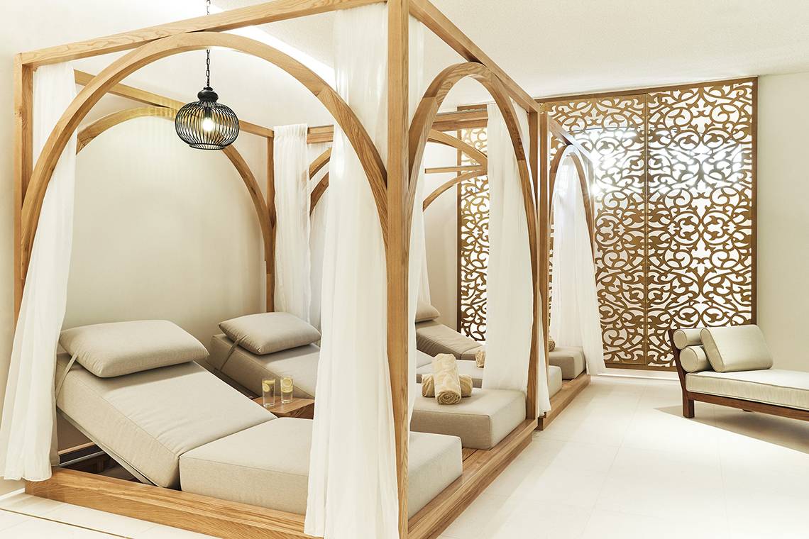 Spa-Lounge-Bereich im Raffles The Palm Dubai mit hölzernen Liegen, weißen Vorhängen und einer goldenen Wand.