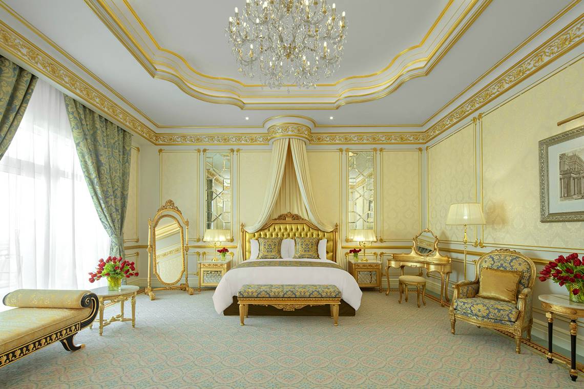 Schlafzimmer im Raffles The Palm Dubai mit goldenen Akzenten und Kristallkronleuchter.