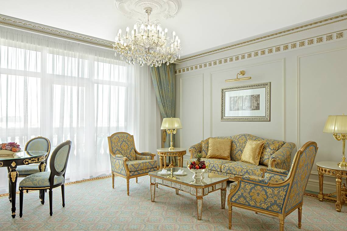 Wohnzimmer im Raffles The Palm Dubai Hotel mit Kristallkronleuchter, goldenen Möbeln und Früchtekorb auf dem Tisch.