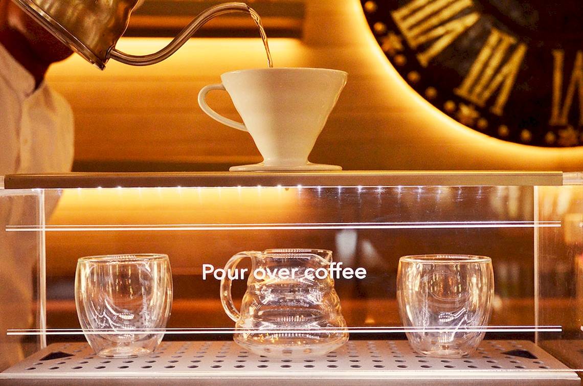Kaffee wird in ein Glas gegossen, während eine Kanne und zwei Gläser darauf warten.