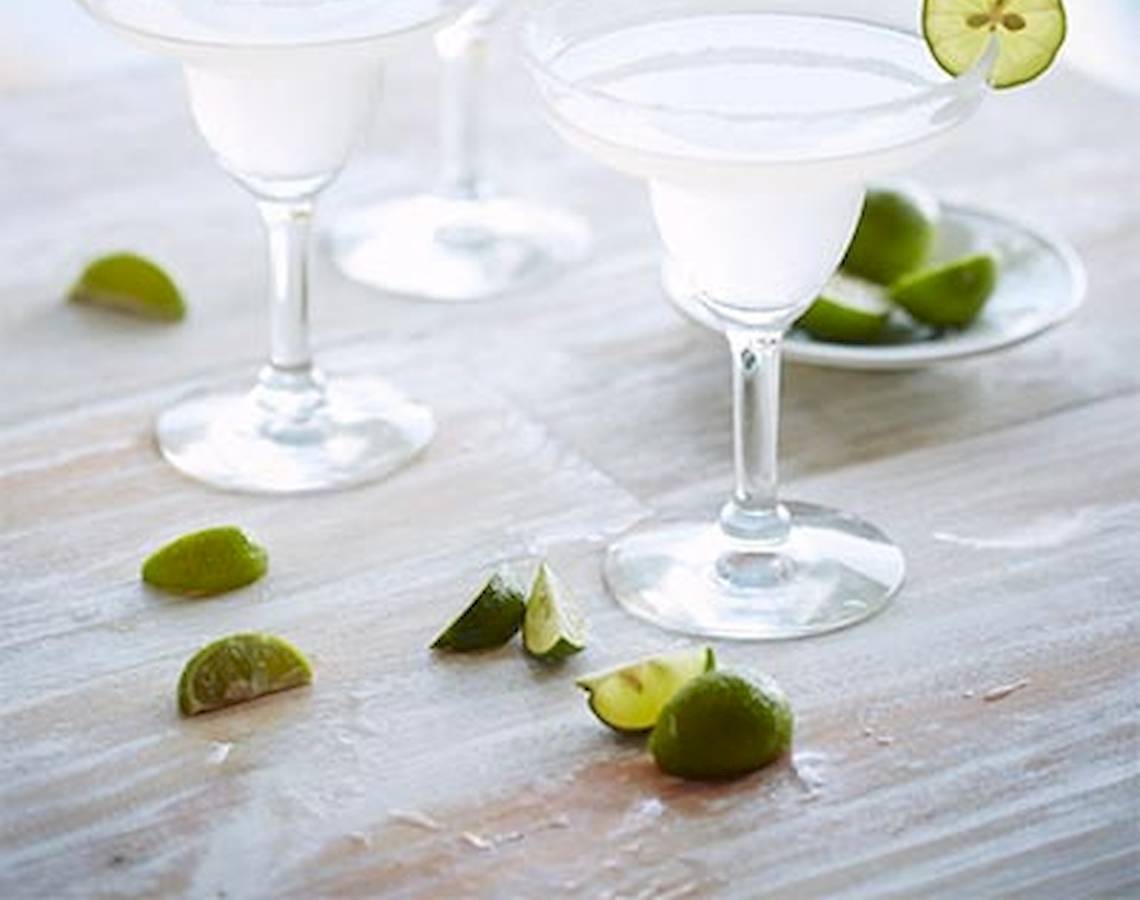 Drei Cocktails mit Limettenscheiben auf einem Holztisch.