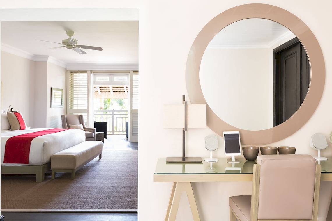 Innenansicht eines Zimmers im LUX Belle Mare Resort & Villas mit Bett, Schreibtisch und Spiegel.
