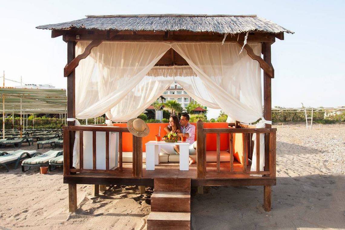 Paar auf einem orangefarbenen Sofa in einem Pavillon am Strand im Orange County Belek Hotel.