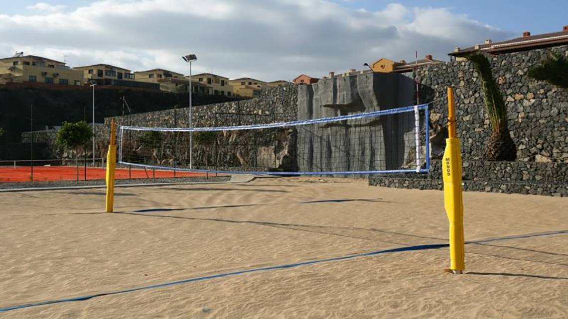 Ein Volleyballnetz auf einem Sandstrand mit einer Steinmauer im Hintergrund.