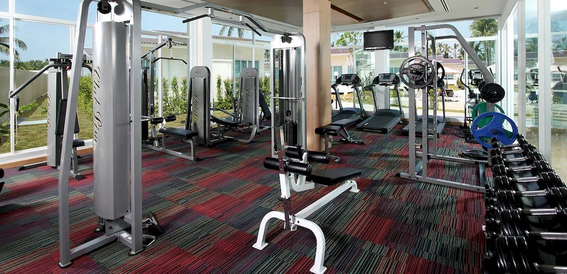 Fitness-Center im Kantary Beach Hotel mit verschiedenen Geräten und großen Fenstern.
