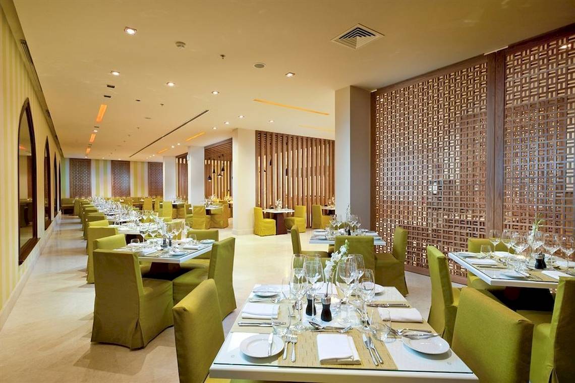Innenbereich des Restaurants im Juweira Boutique Hotel mit grünen Stühlen und Tischen.