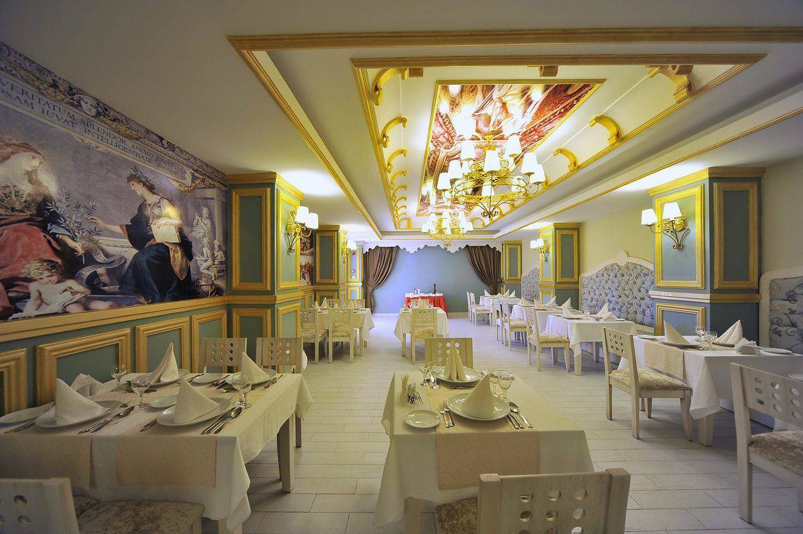 Innenansicht des Restaurants im Seaden Corolla Hotel mit kunstvollen Deckengemälden, Tischdekorationen und geometrischen Wandmustern.