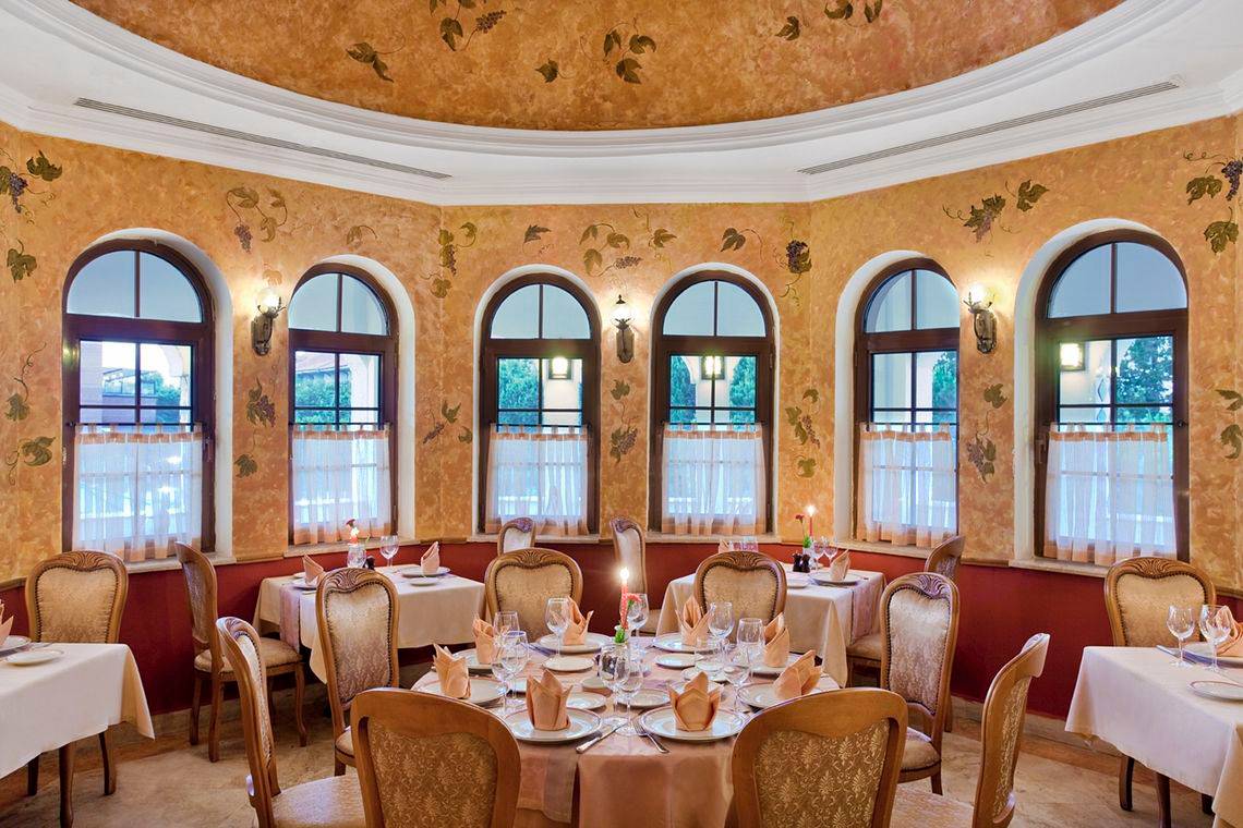 Innenansicht des Restaurants im Kremlin Palace Hotel mit runden Fenstern und gedeckten Tischen.
