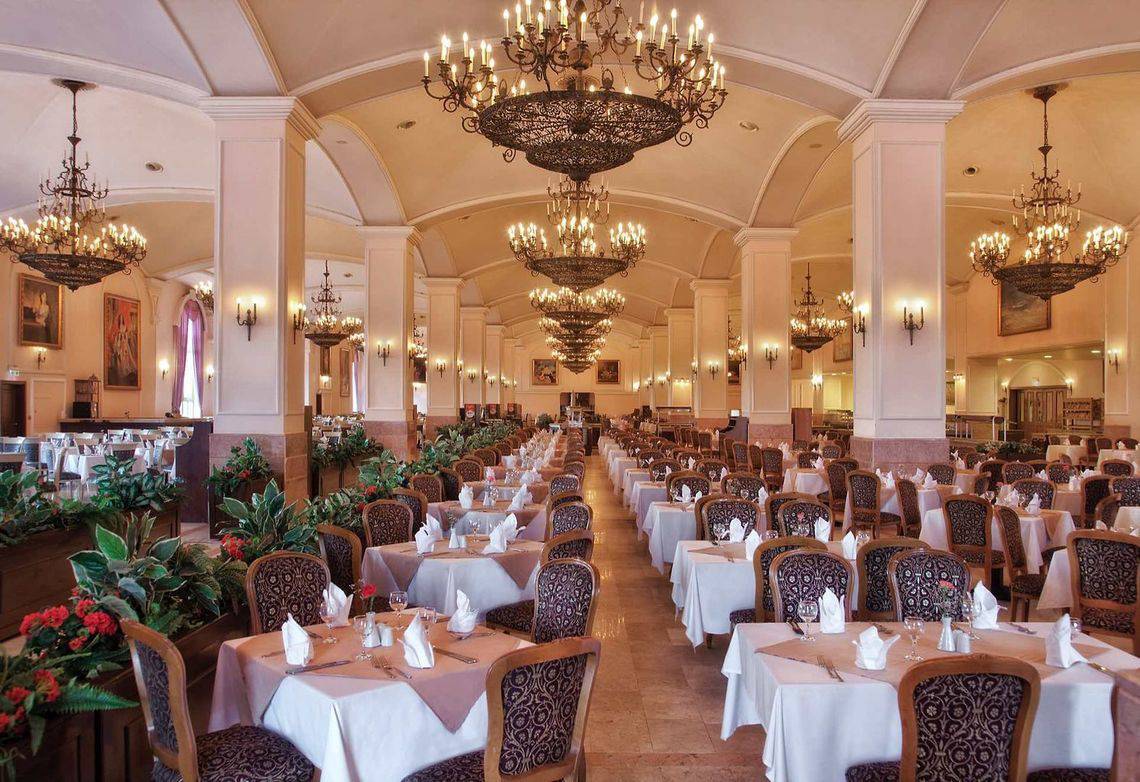 Restaurant im Kremlin Palace Hotel mit gedeckten Tischen und Kronleuchtern.
