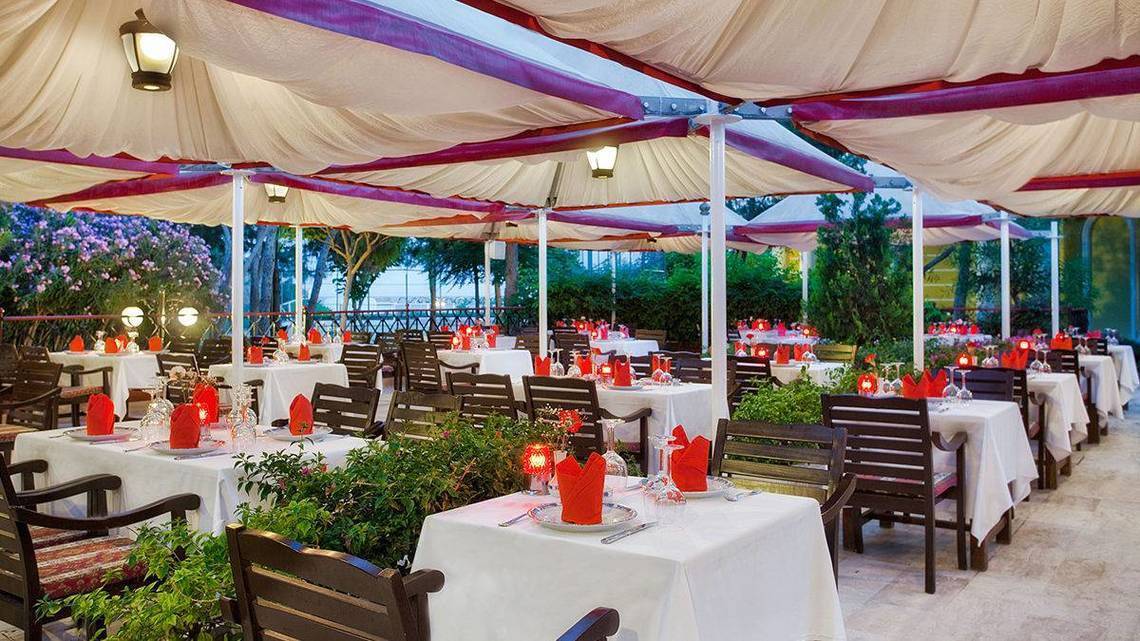 Überdachtes Restaurant des Kremlin Palace Hotels mit gedeckten Tischen und roten Tischtüchern.