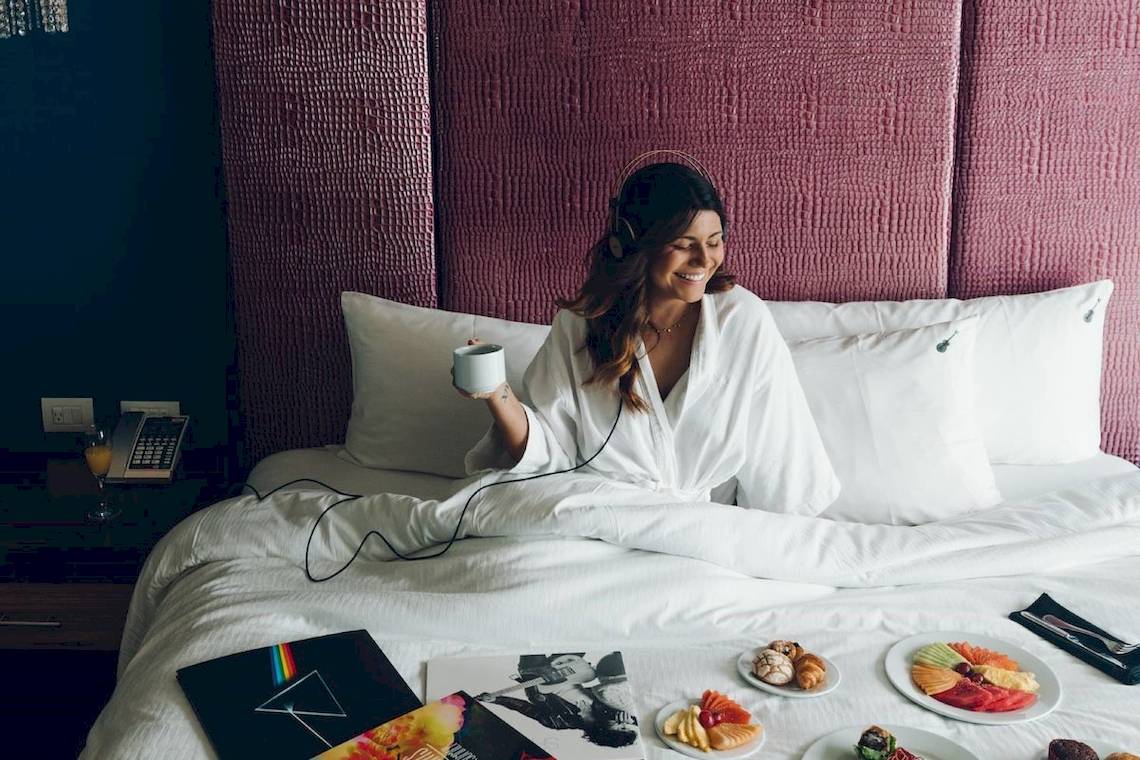 Frau im weißen Bademantel im Bett mit Frühstück und Kopfhörern im Hard Rock Hotel Cancun