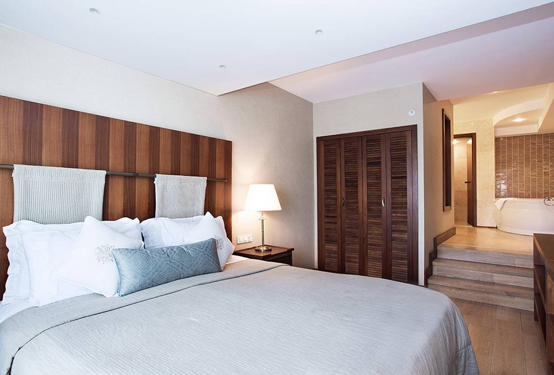 Schlafzimmer im Marti Resort mit einem großen Bett, weißen Kissen, einer Lampe und einem Badezimmer mit Badewanne.