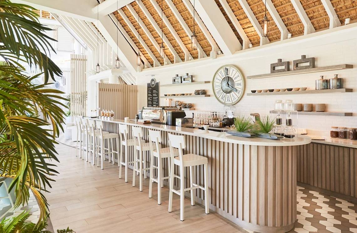 Innenansicht der Rezeption des LUX Grand Gaube Resort & Villas mit Bar, Uhr und Pflanzen.