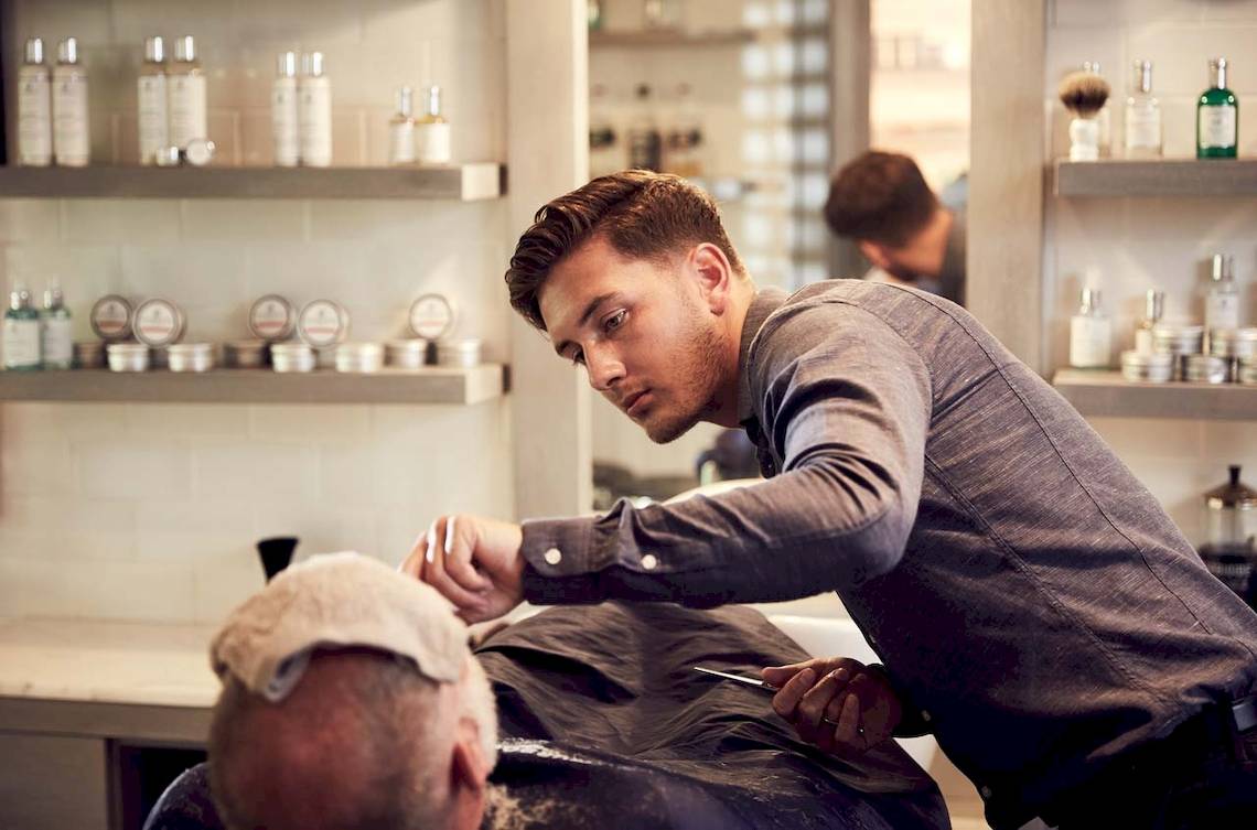 Friseur in einem Salon, der einen älteren Mann rasiert