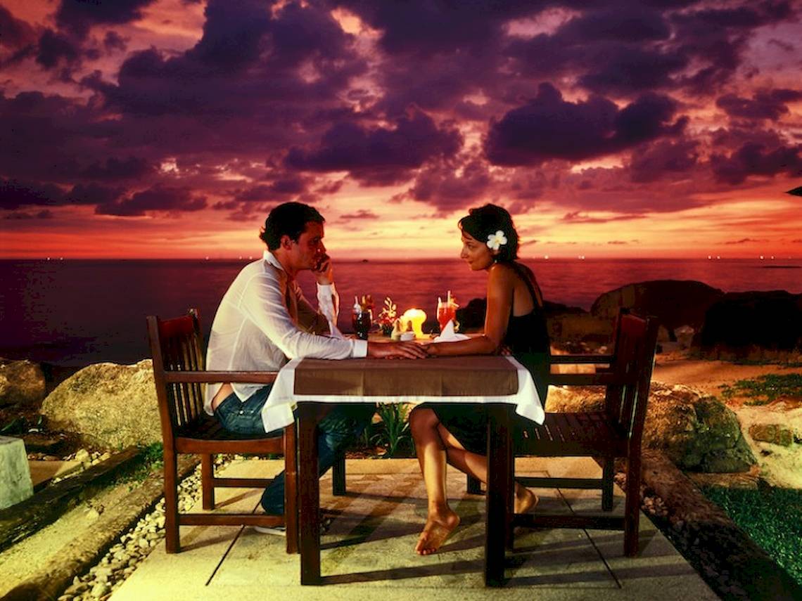 Paar beim Abendessen am Strand unter einem farbenfrohen Himmel