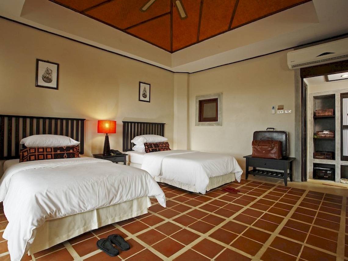 Zwei Betten mit weißen Laken und Kissen in einem Hotelzimmer mit braunen Fliesen und Dekoration.