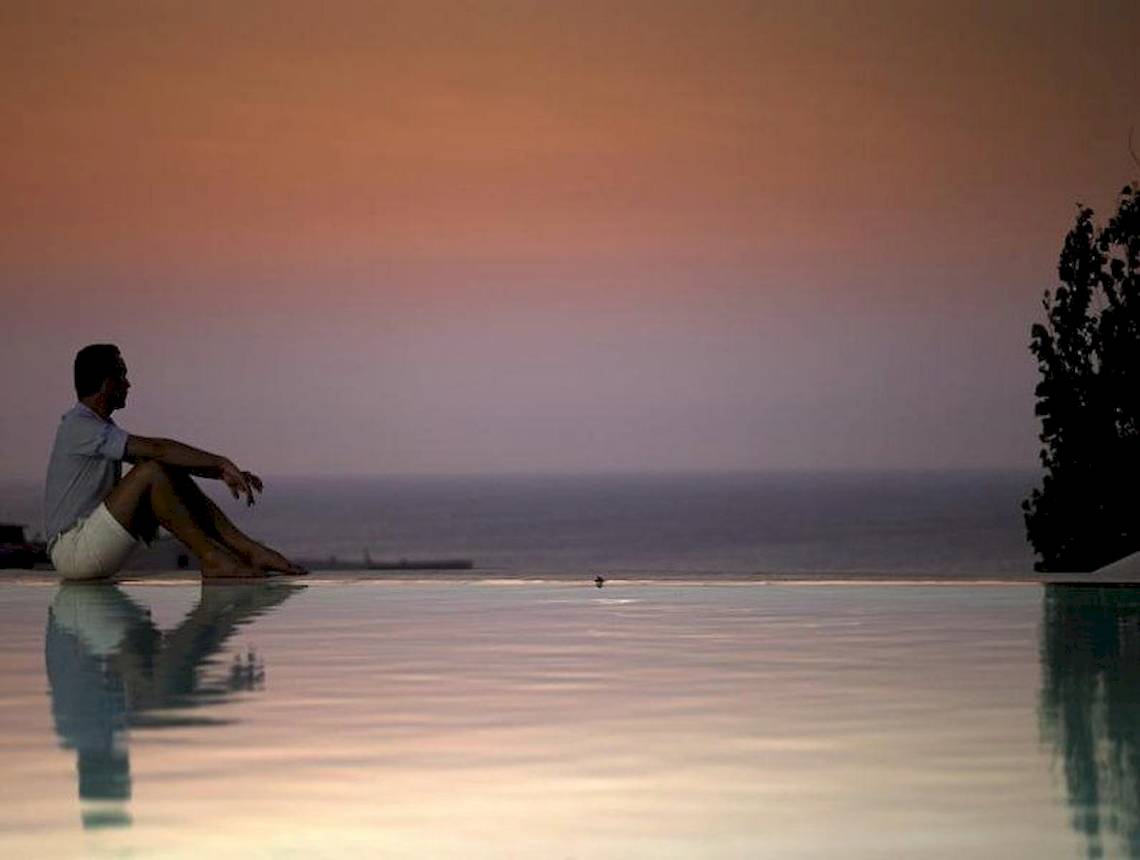 Mann sitzt am Poolrand und genießt den Sonnenuntergang am Meer.