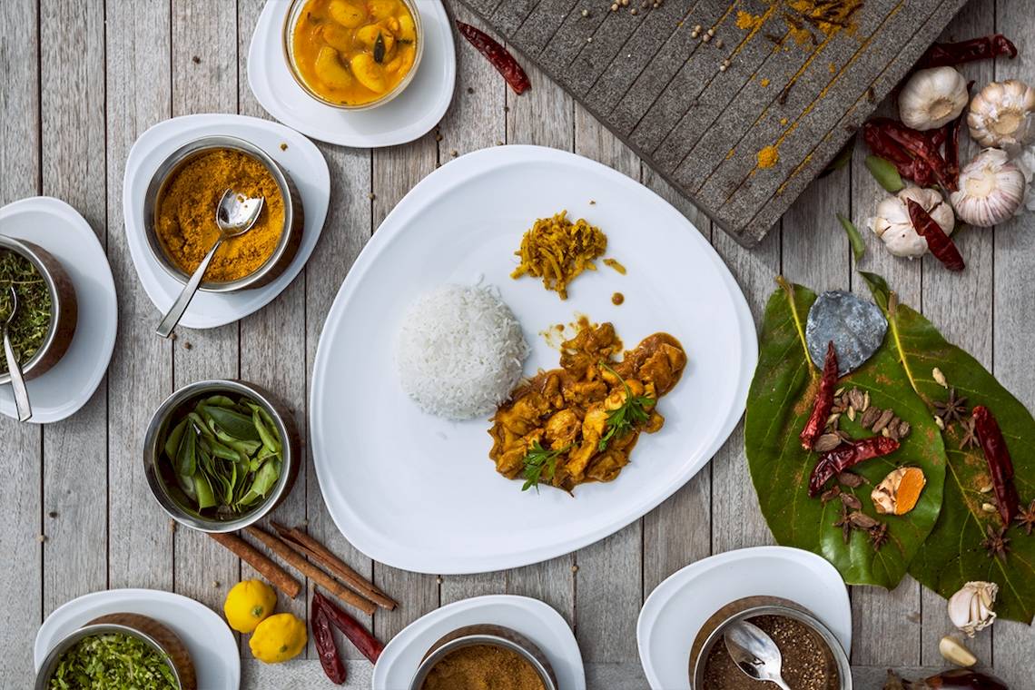 Ein Gericht mit Curry und Reis auf einem Holztisch, umgeben von Gewürzen und Zutaten.
