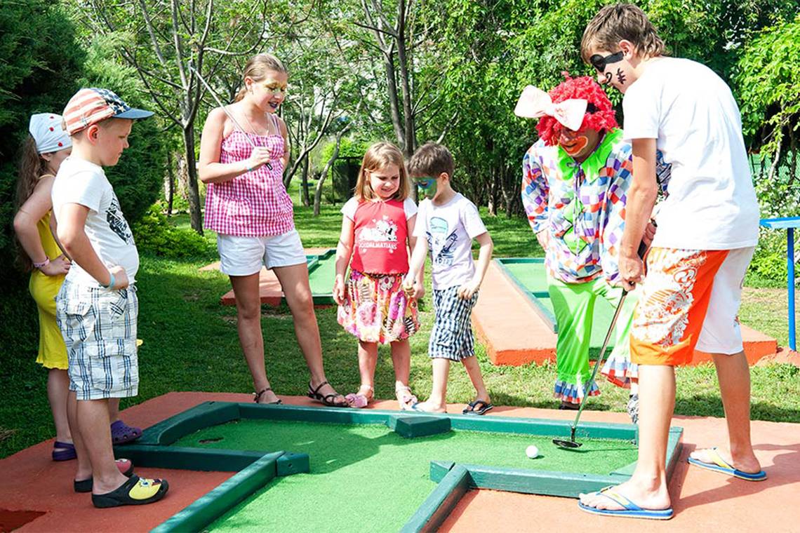 Kinder spielen Golf im Freien am Belconti Resort mit Clowns als Begleiter.
