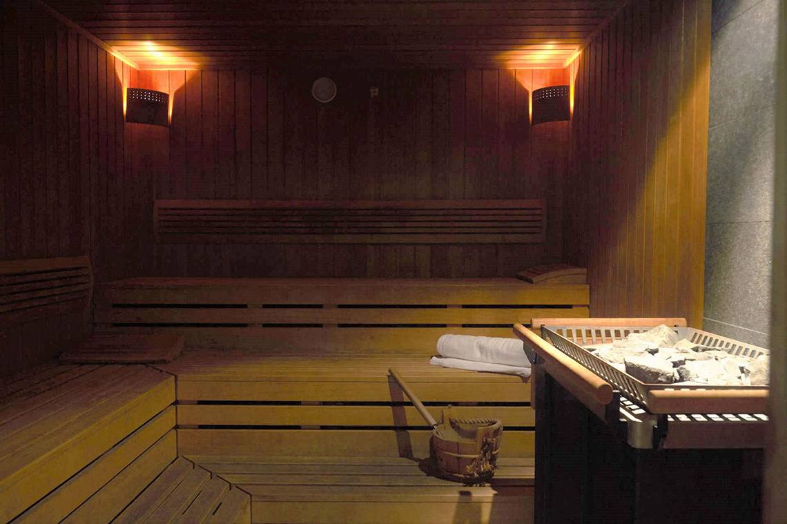 Saunaraum im Capo Bay Hotel mit Holzbänken, einer Wanduhr und hellen Lichtern.