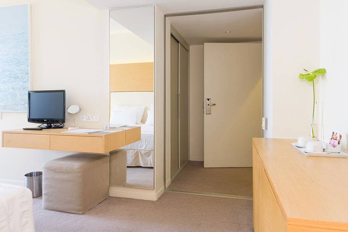 Inneneinrichtung eines Zimmers im Capo Bay Hotel mit Schreibtisch, Spiegel, Pflanzen und Betten.