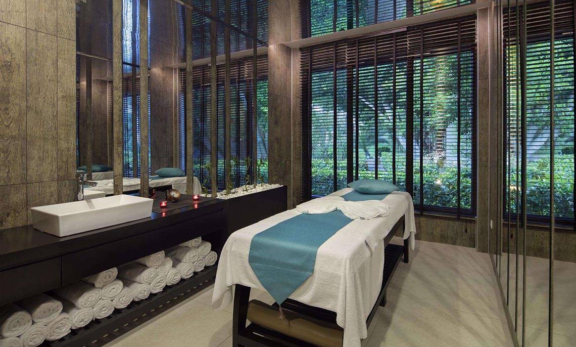 Spa-Behandlungsraum im Magic Life Belek Hotel mit Massageliege, Waschbecken und Blick auf den Garten.