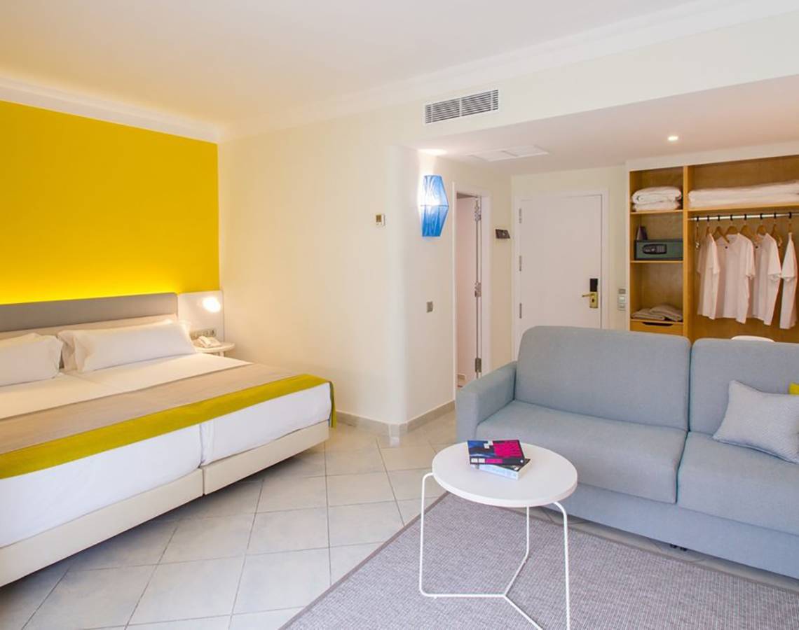 Innenansicht eines Zimmers im Abora Catarina Hotel mit Bett, Sofa, Tisch und Kleiderschrank.