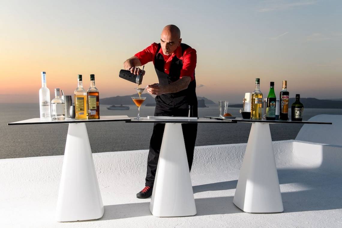 Ein Barkeeper bereitet einen Cocktail auf einer weißen Tischplatte bei Sonnenuntergang zu.