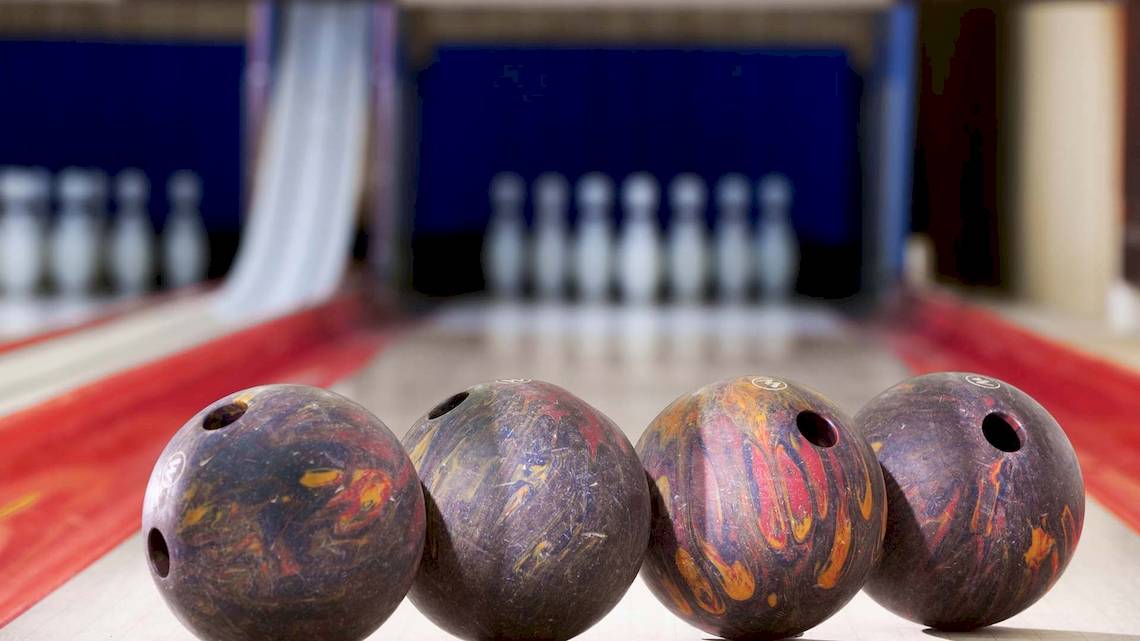 Vier Bowlingkugeln auf einer Bowlingbahn mit Bowlingkegeln im Hintergrund.
