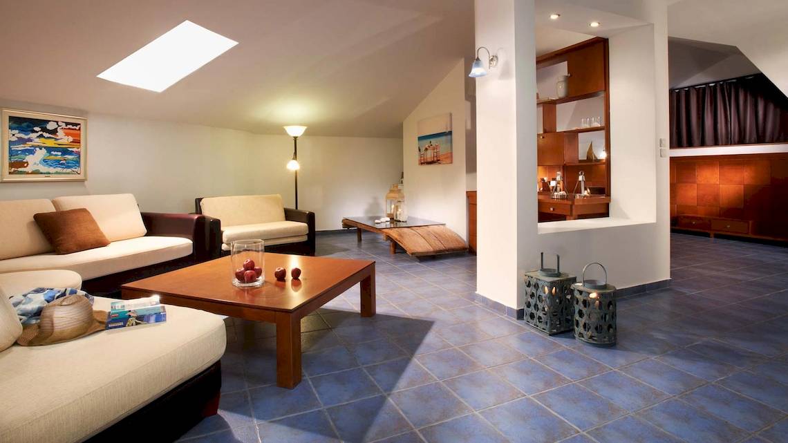 Innenansicht des Acrotel Athena Pallas Hotels mit Wohnzimmer, Couch, Tisch, Lampe und Dekoration.