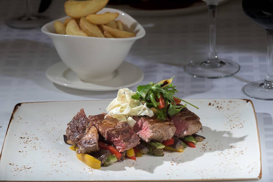 Ein Teller mit gebratenem Steak, Gemüse und Kartoffeln auf einem Tisch.