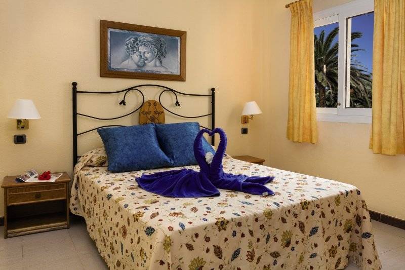 Hotelzimmer mit Bett, blauem Handtuch als Schwan, und Blick auf Palmen draußen
