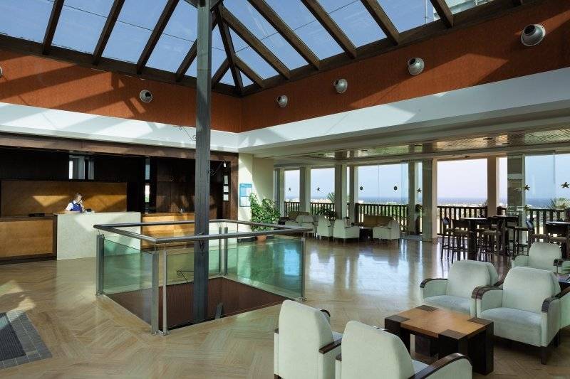Lobby des Club Caleta Dorada Hotels mit Empfangstresen, Sitzbereich und Glaswänden.