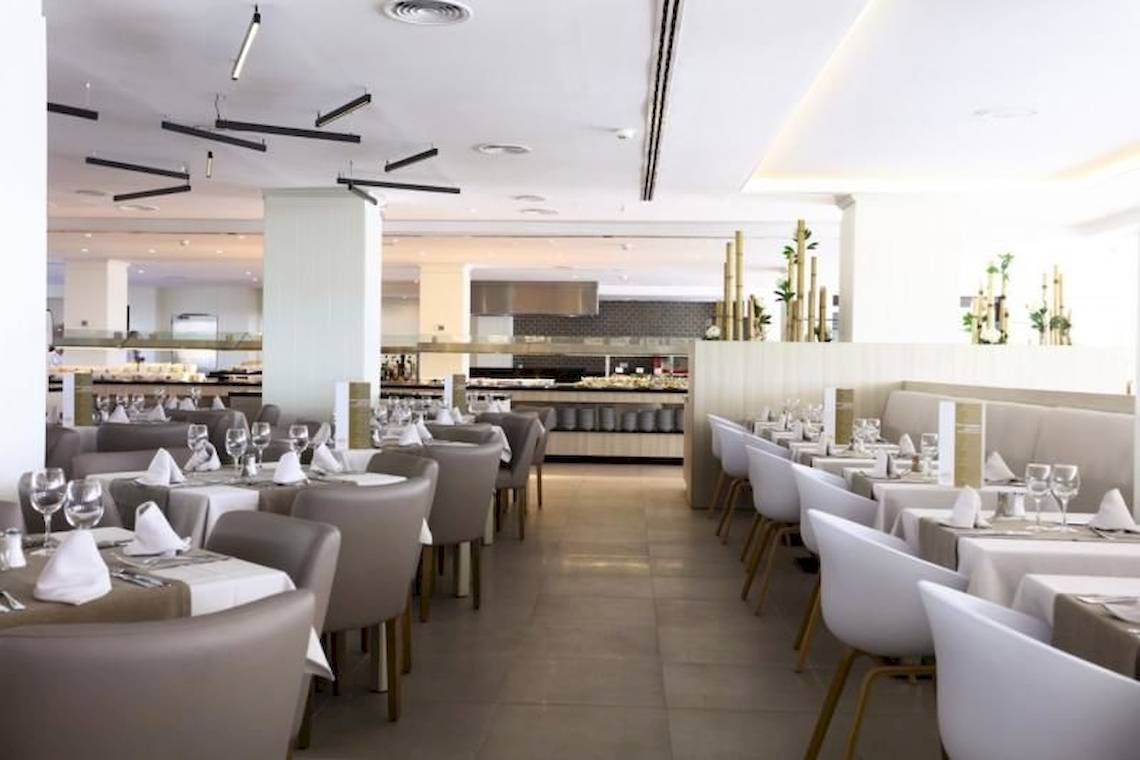 Restaurant im Playa Golf Hotel mit gedeckten Tischen und Stühlen, serviertem Geschirr und einem offenen Küchenbereich.