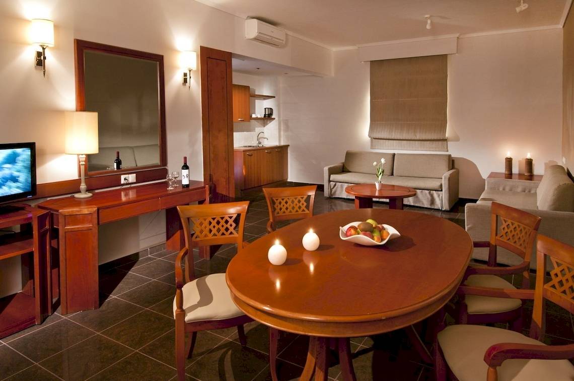 Innenbereich des Kipriotis Village Resort mit Esstisch, Stühlen, Sofa, Fernseher und Dekorationsgegenständen.