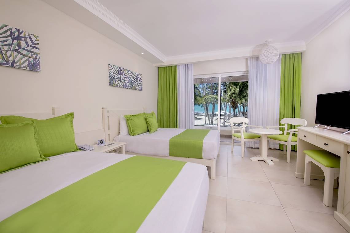 Zimmer im Vista Sol Punta Cana Beach Resort & Spa mit zwei Betten und grünen Kissen.