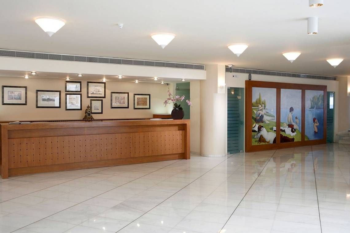 Empfangsbereich des Aquila Porto Rethymno Hotels mit Holzrezeption und Gemälden an der Wand.