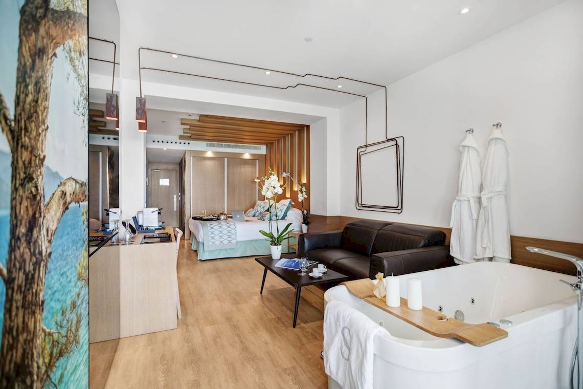 Innenansicht eines Hotelzimmers von Pure Salt Garonda mit Bett, Badewanne und Wohnzimmerbereich.