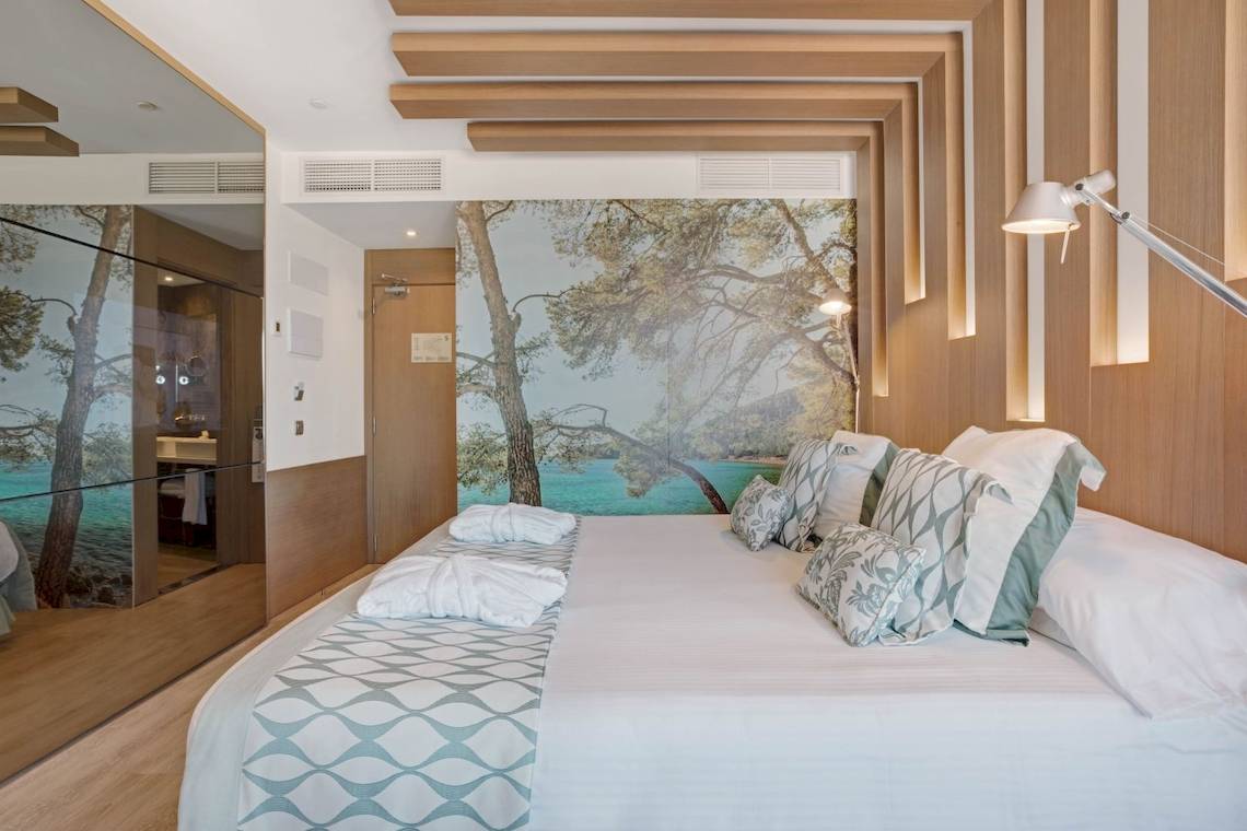 Schlafzimmer im Pure Salt Garonda Hotel mit Bett, Kissen und Panoramawandbild am Meer.