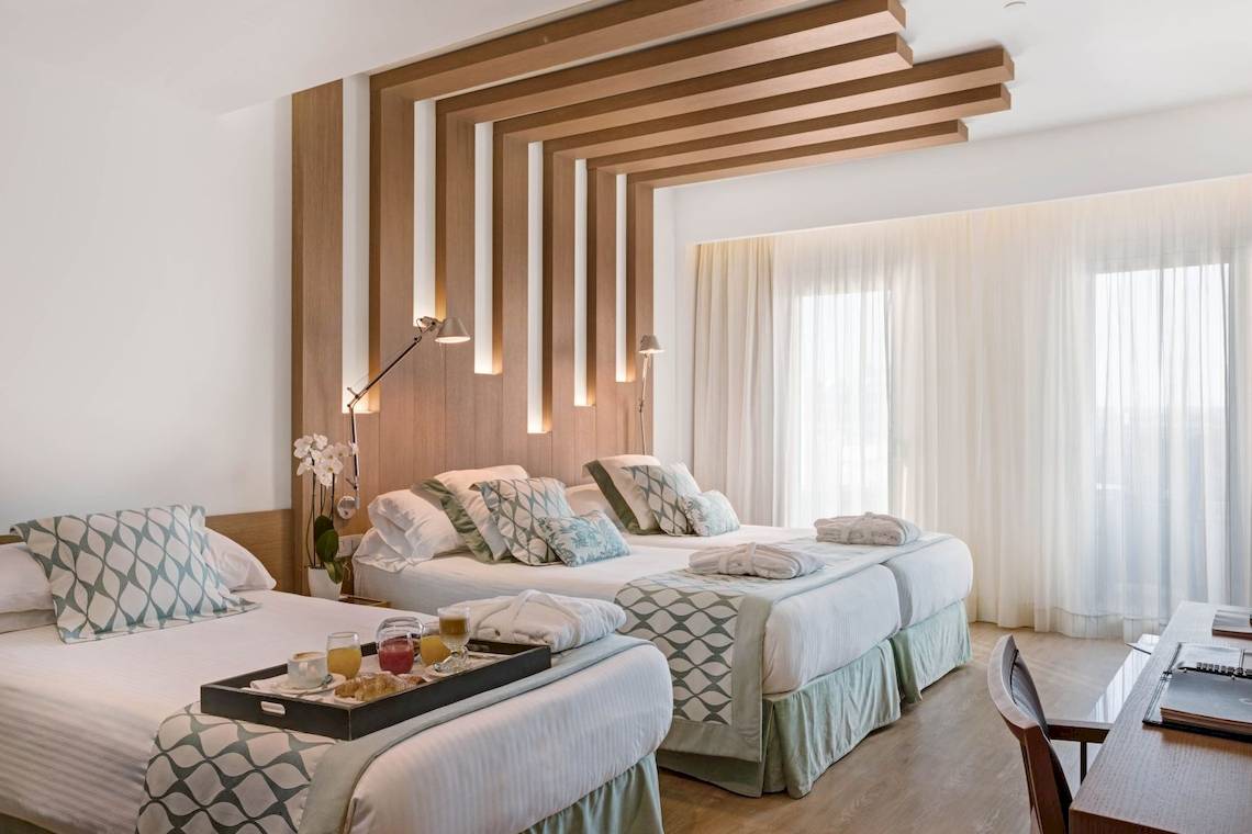 Hotelzimmer von Pure Salt Garonda mit drei Betten, Frühstückstablett und Fenstern.