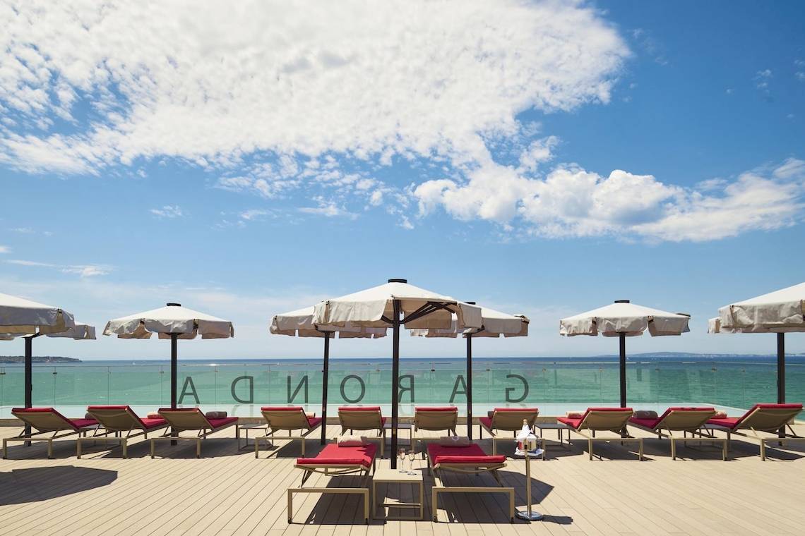 Außenbereich des Pure Salt Garonda Hotels mit Liegen, Sonnenschirmen und Meerblick.