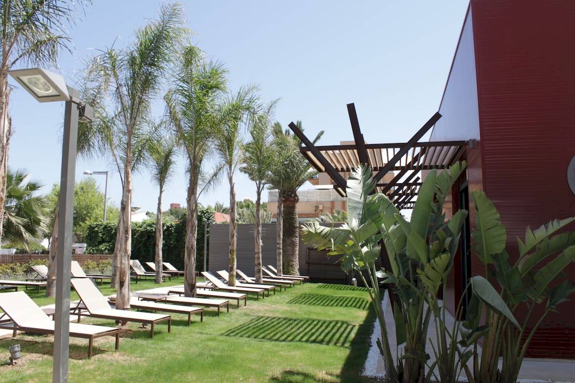 Außenbereich des Pure Salt Garonda Hotels mit Liegen, Palmen und einer Pergola.