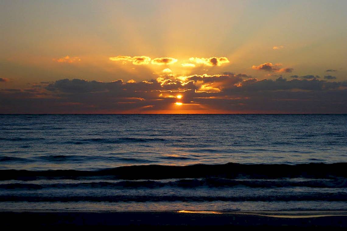 Sonnenuntergang am Strand mit Meer und Wolken, goldene Sonne hinter den Wolken.