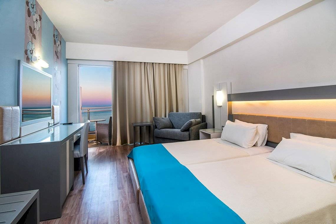 Zimmer im Pegasos Deluxe Beach Hotel mit Meerblick, Bett, Schreibtisch und Sofa.