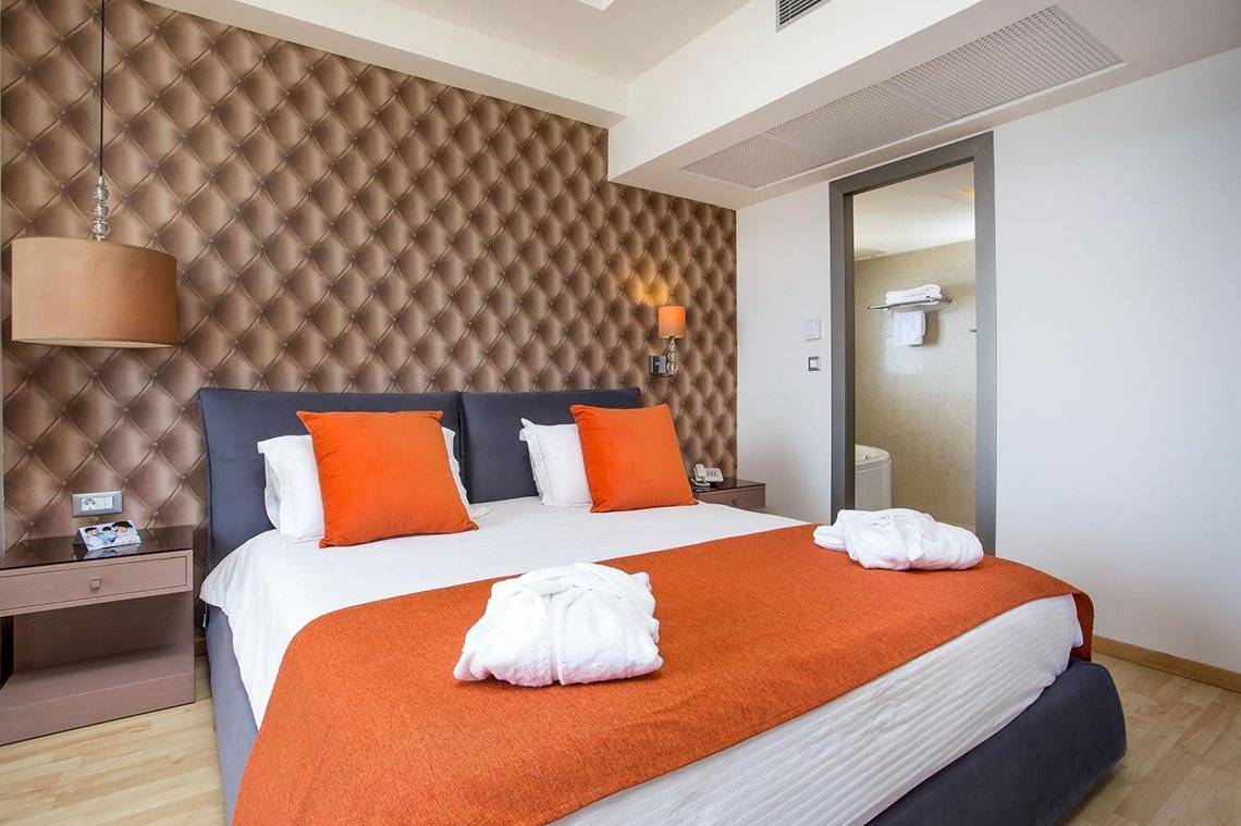 Schlafzimmer im Pegasos Deluxe Beach Hotel mit orangen Kissen und einem Bett.